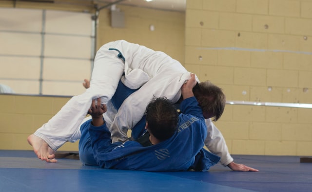 Judo sport. A photo of two men who are practicing Judo. One man is wearing a white Judo uniform and another man is wearing a blue Judo uniform